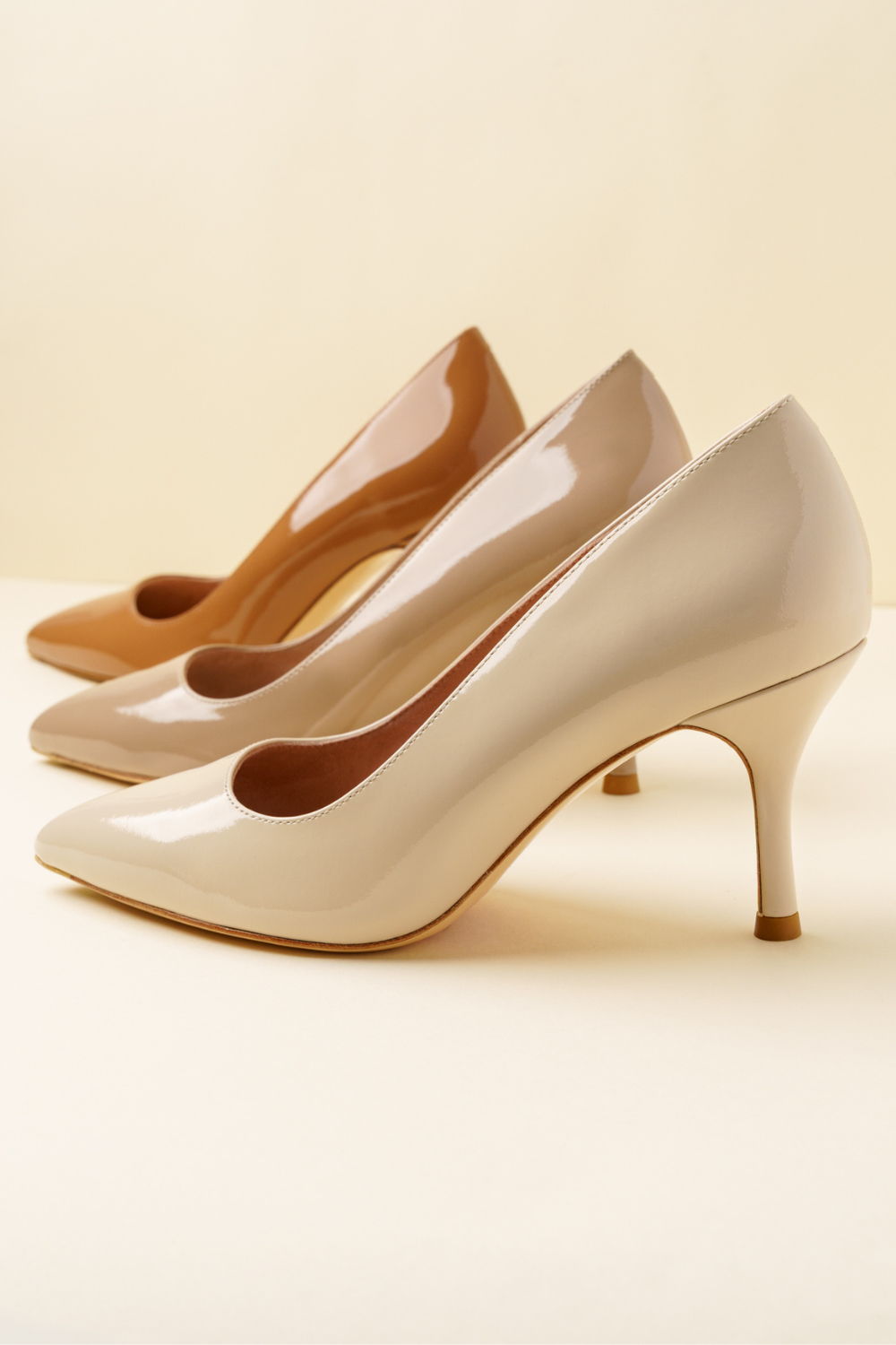Three pairs of high-heeled shoes in different shades on a neutral background.