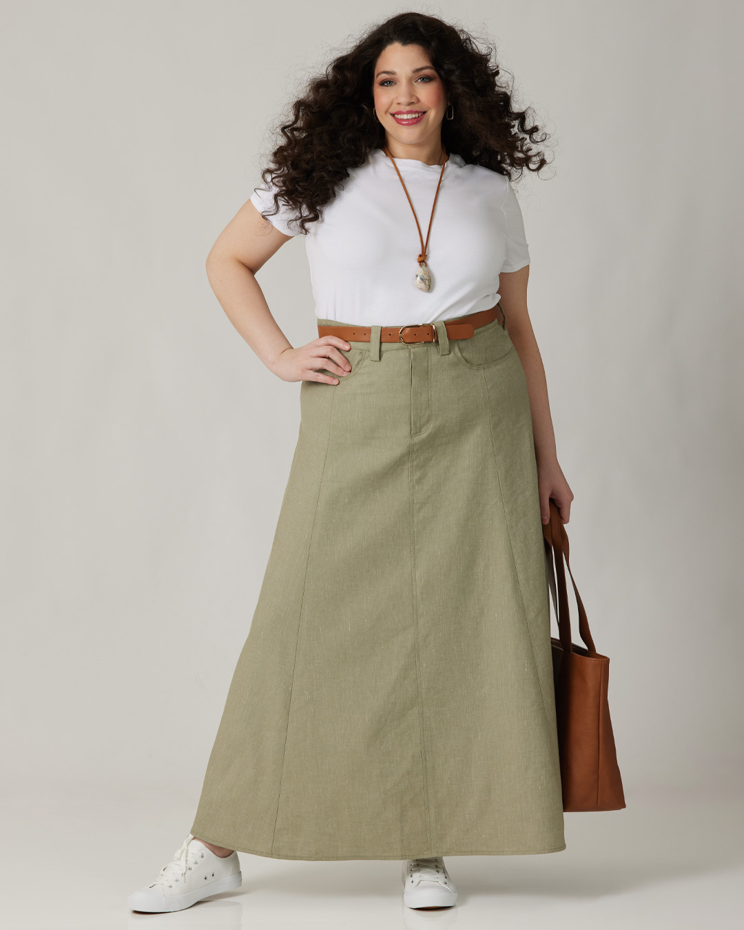A woman in a white shirt and green skirt, holding a brown bag.