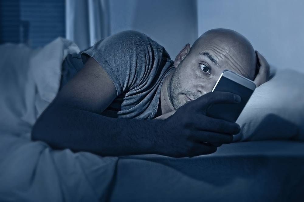 image of a man checking his phone in bed