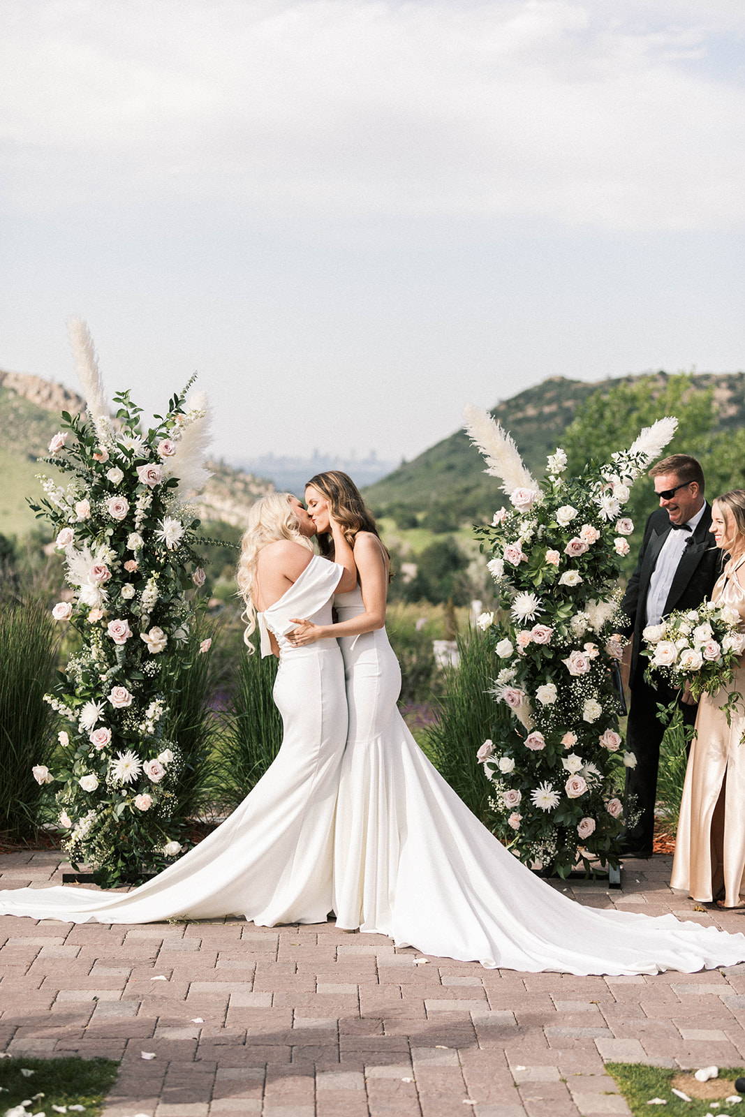 Brides sharing a kiss in front of white floral arbor