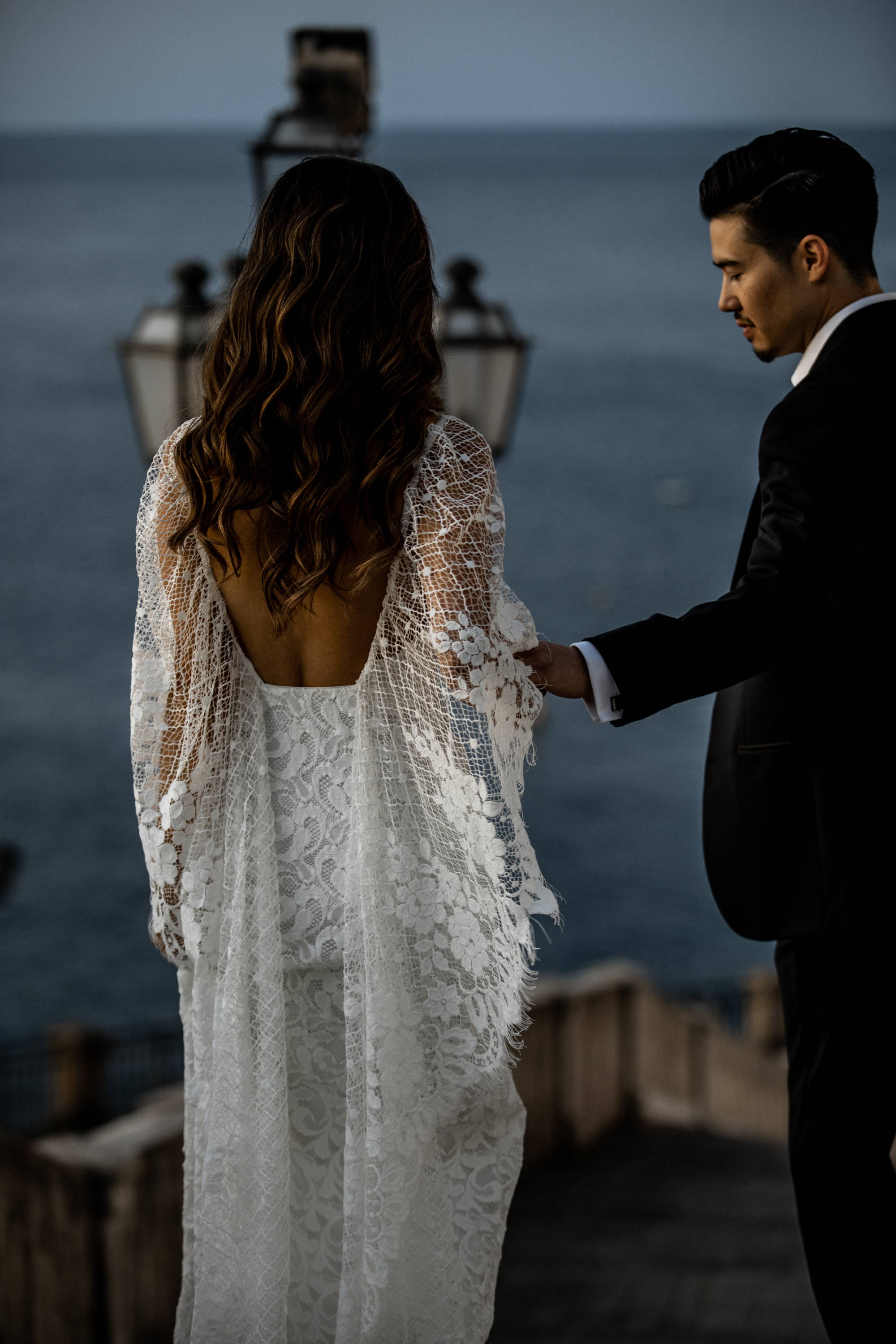 Bride wearing a lace dress draping over the shoulder with her groom wearing a black suit
