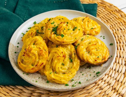 A plate of golden, spiraled potato pastries garnished with herbs.