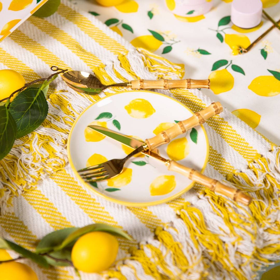 A festive table setting featuring a lemon-print tablecloth and bamboo cutlery with golden accents, accompanied by a plate with lemon graphics.