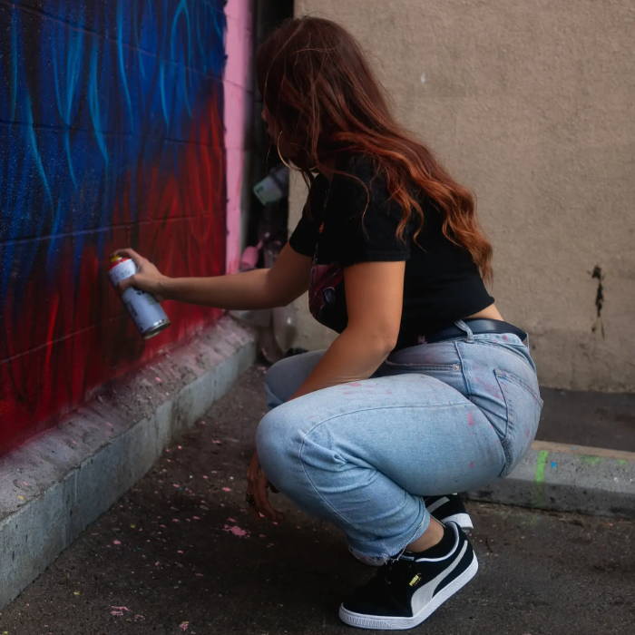 woman spray painting wall in puma suede classic shoes