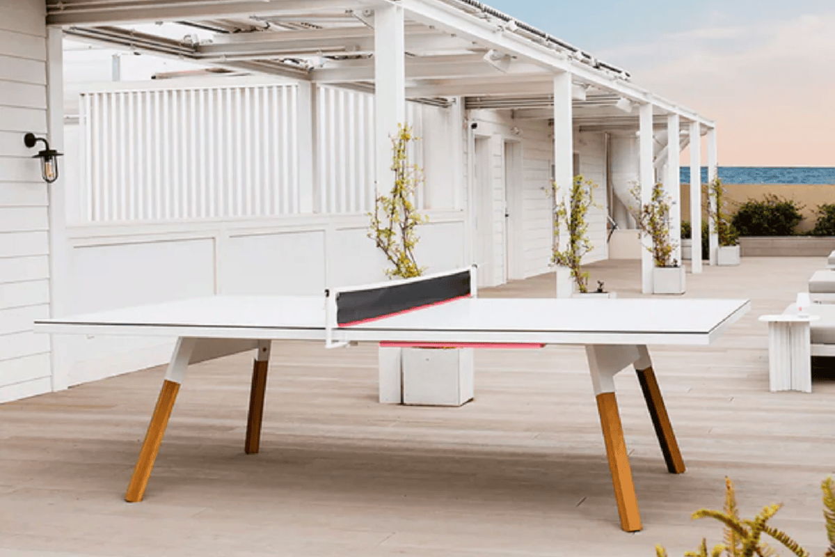 Outdoor ping pong table on a covered coastal terrace with white walls and ocean visible in the distance.