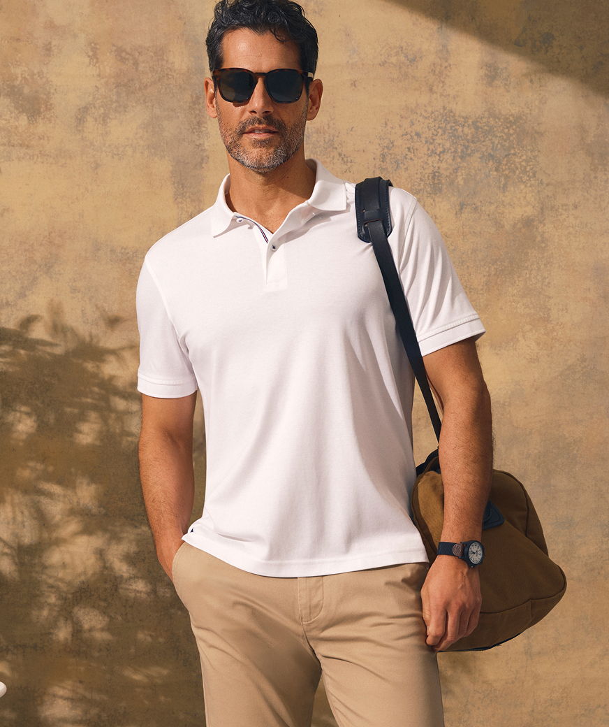 Man in sunglasses wearing a white polo shirt, standing with a bag.