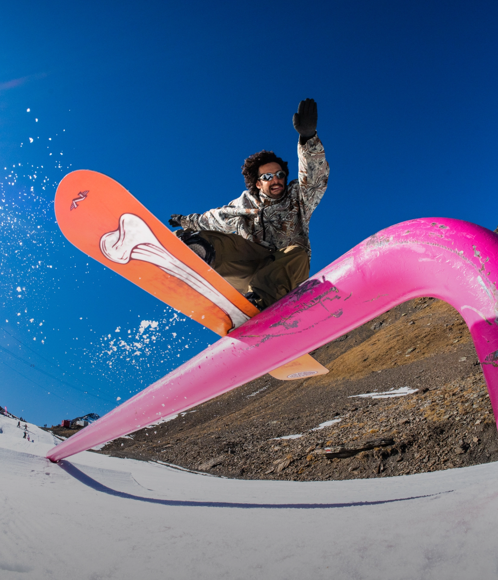 Snowboarder performing a trick on a pink rail against a clear blue sky.