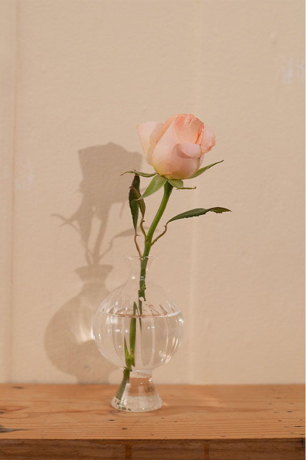 A single pink rose in a clear vase on a wooden surface.
