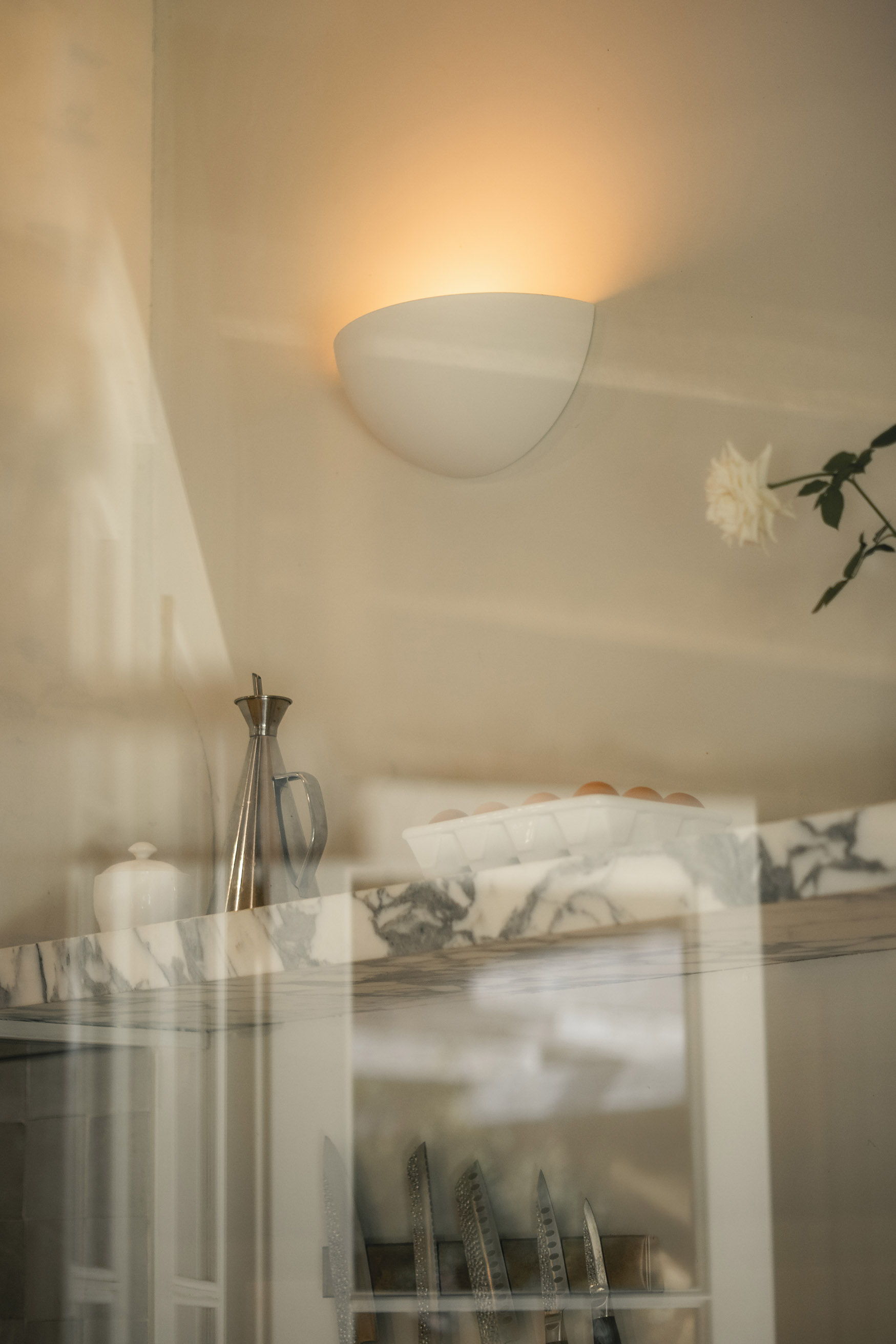A softly lit wall fixture reflecting in a window with decorative items.