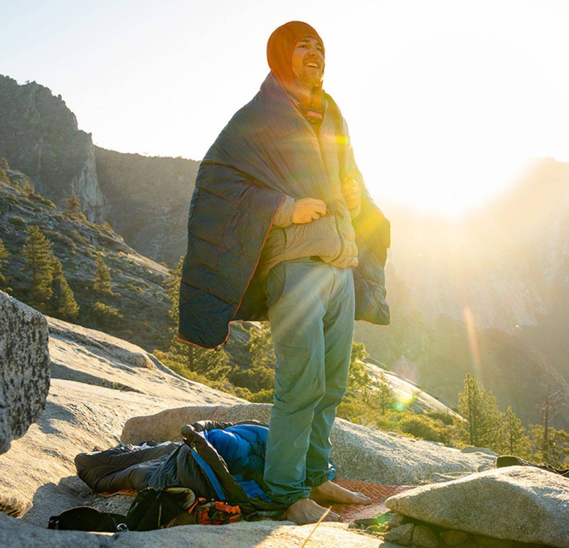 A person on a mountain at sunrise, wearing a Rumpl around his shoulders