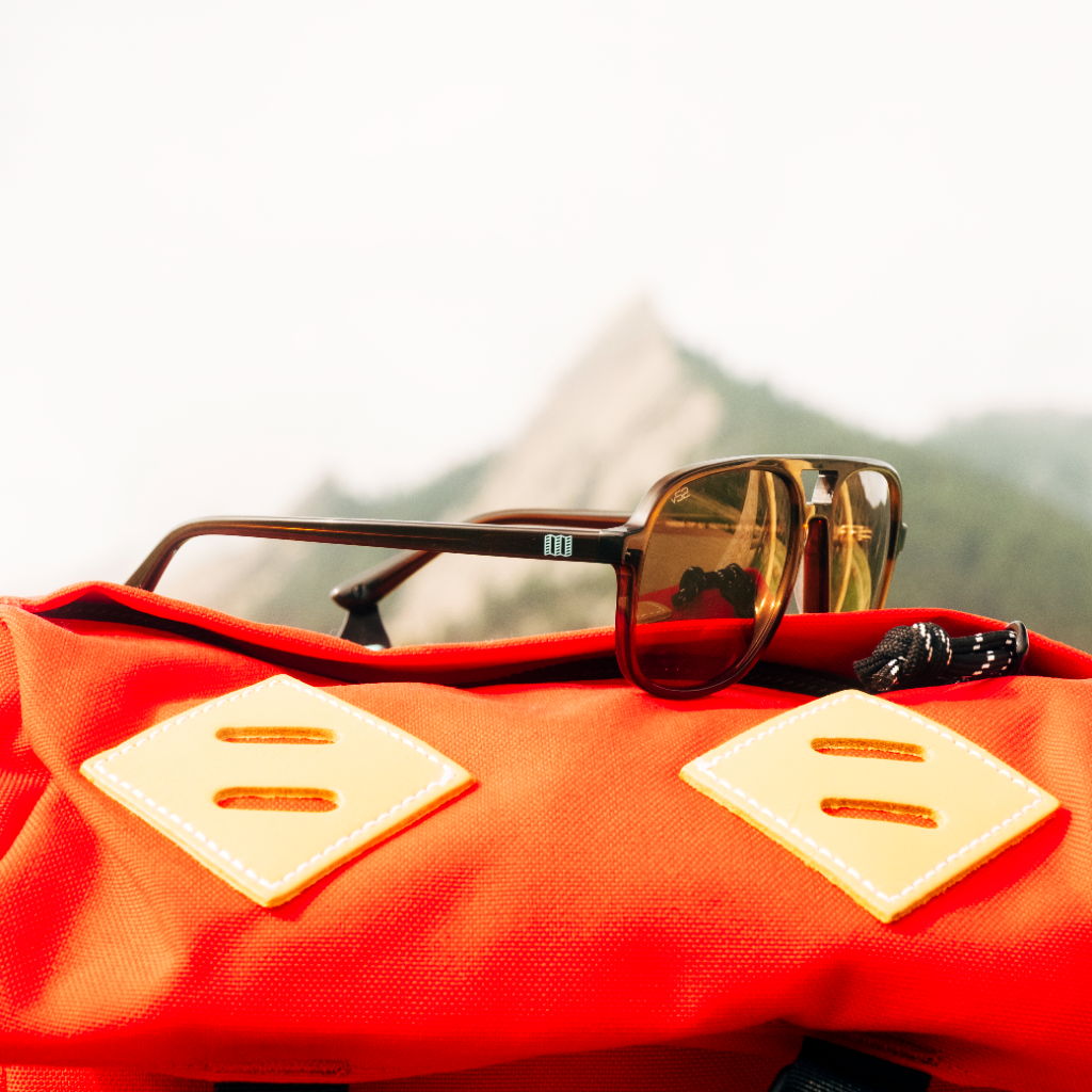 Sunglasses resting on a red backpack with a mountain backdrop.