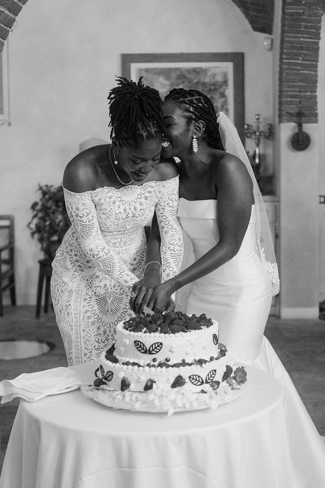 Two brides joyfully cutting their wedding cake together.