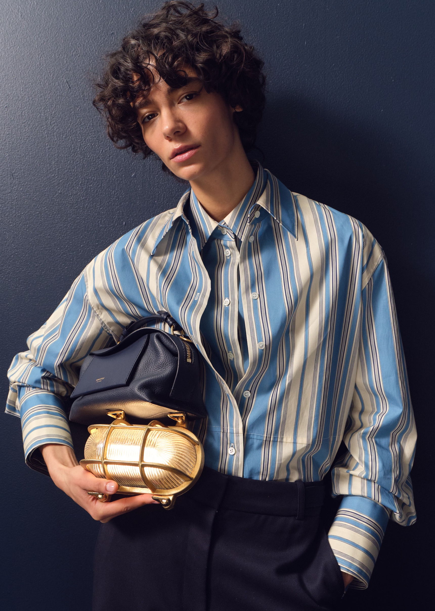 Person in striped shirt holding bags against a dark background.