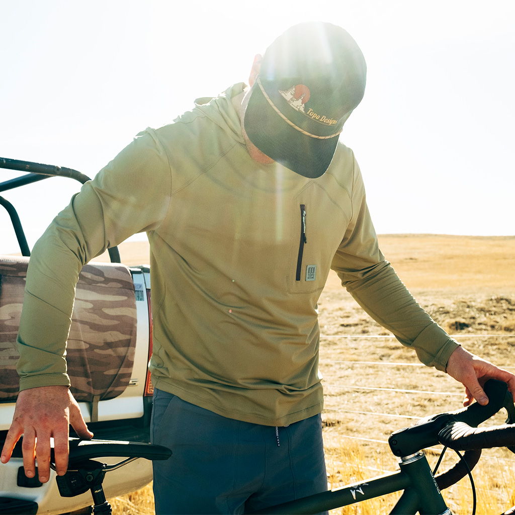 Person adjusting a bicycle near a vehicle in a sunny outdoor setting.