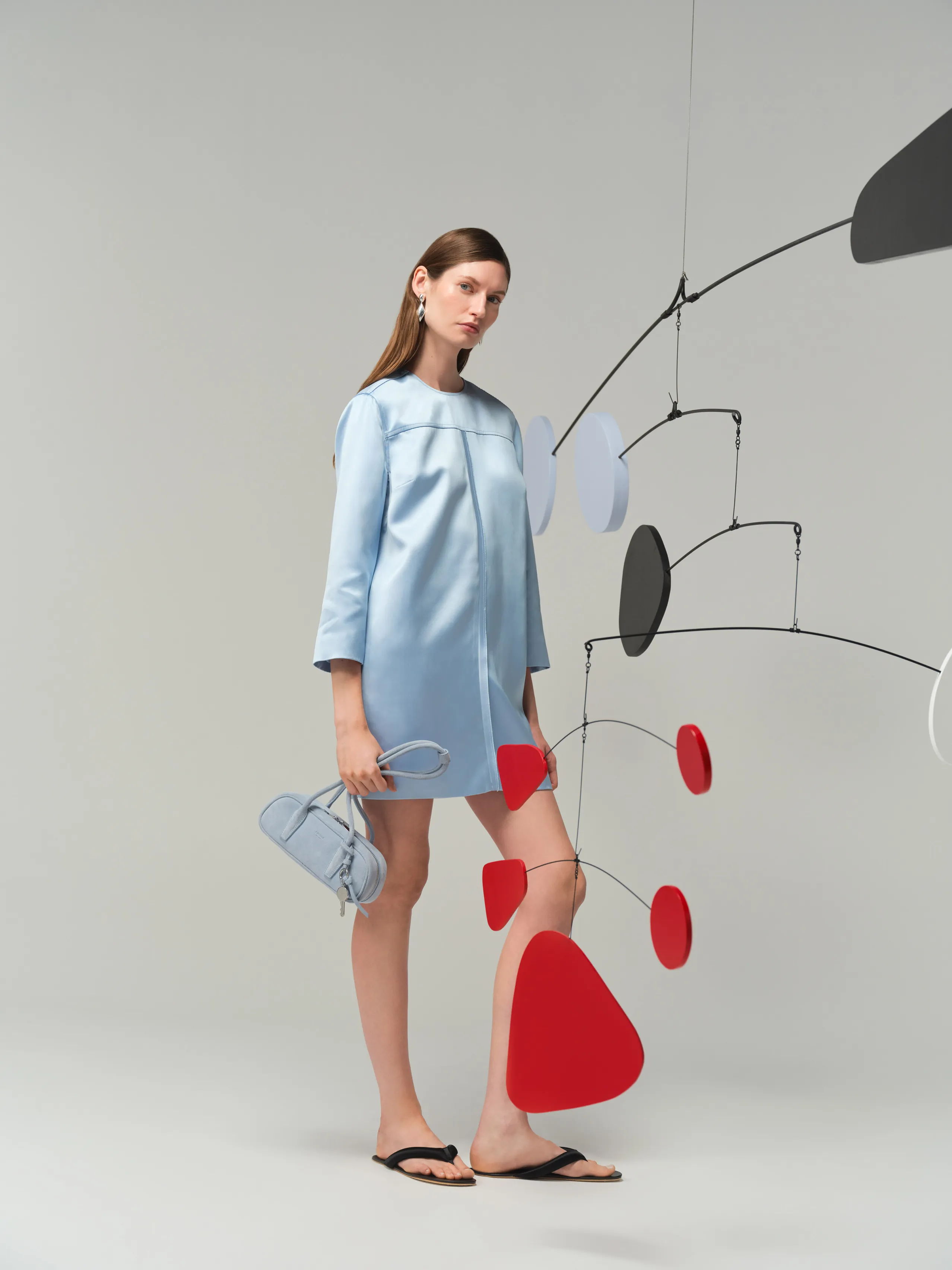 Model in a light blue dress with a mobile sculpture in the background.