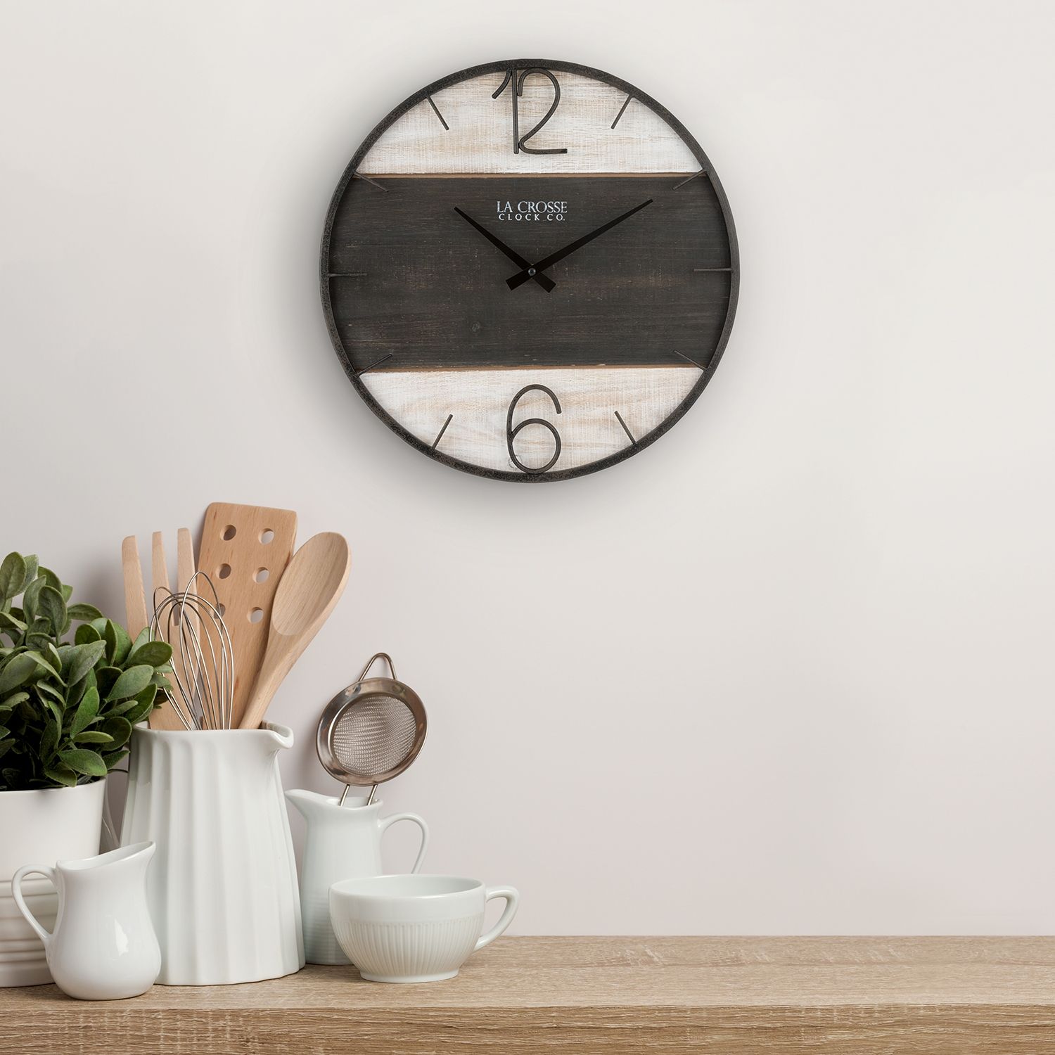 16-inch Ironwood Wall Clock clock above kitchen utensils and white dishware on wooden surface.