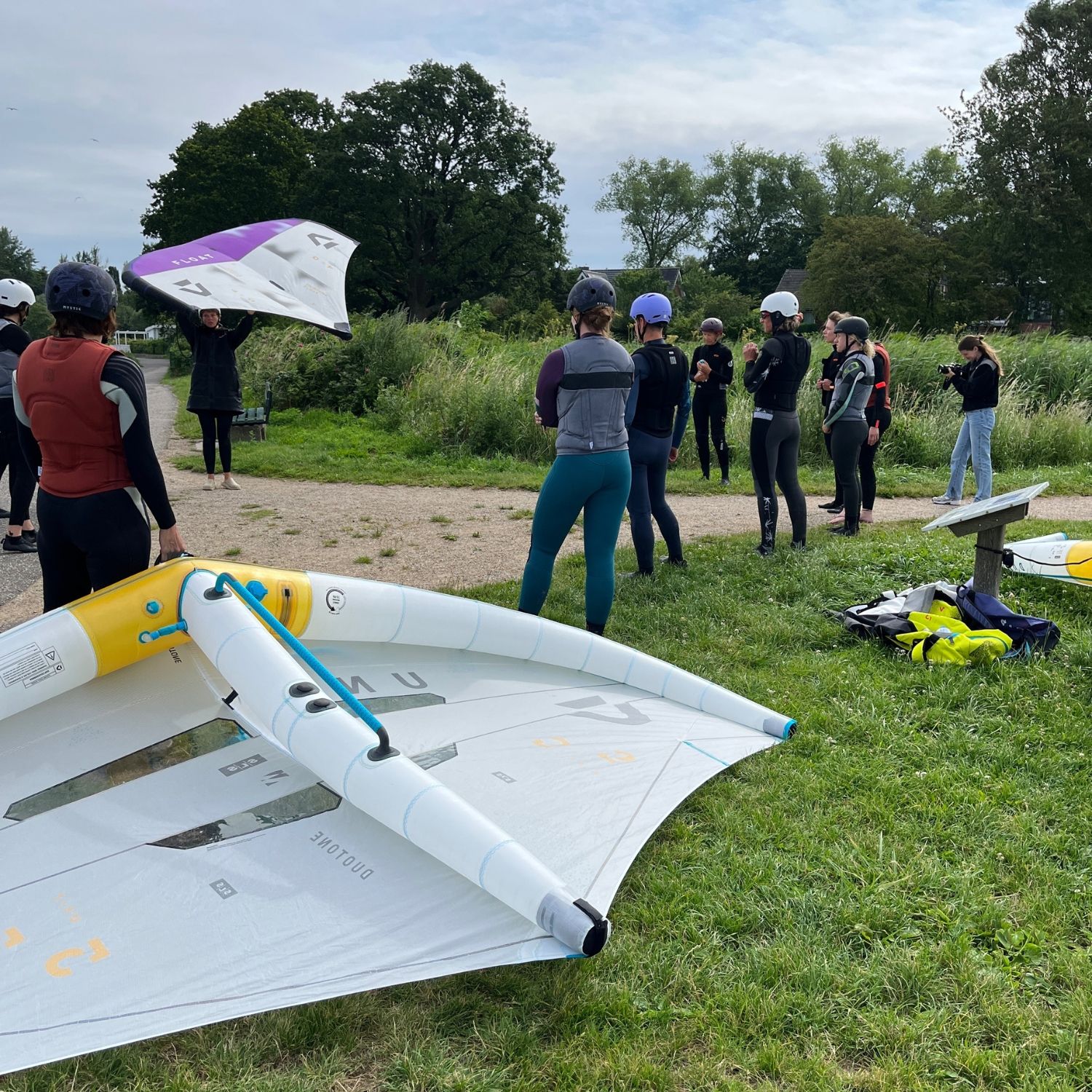 Group of people preparing for wing foiling on a grassy area.