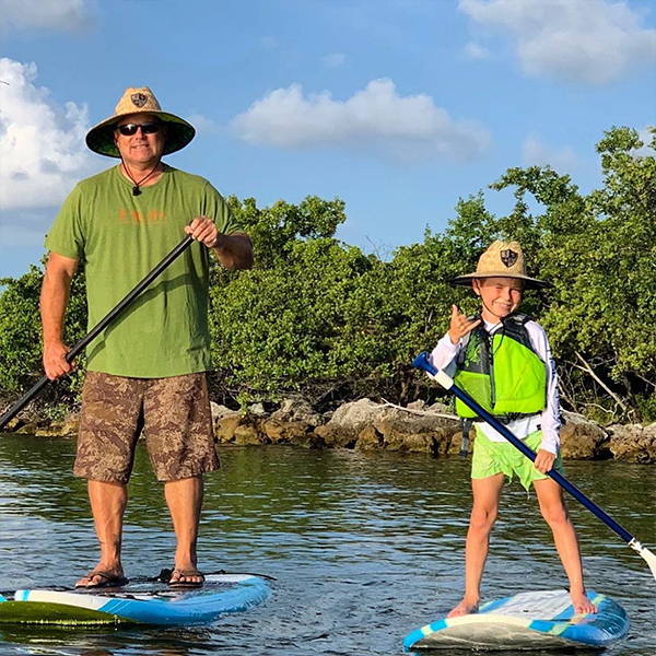 Bosun Lindsey paddle boarding with an adult, both are wearing SA Company straw hats.