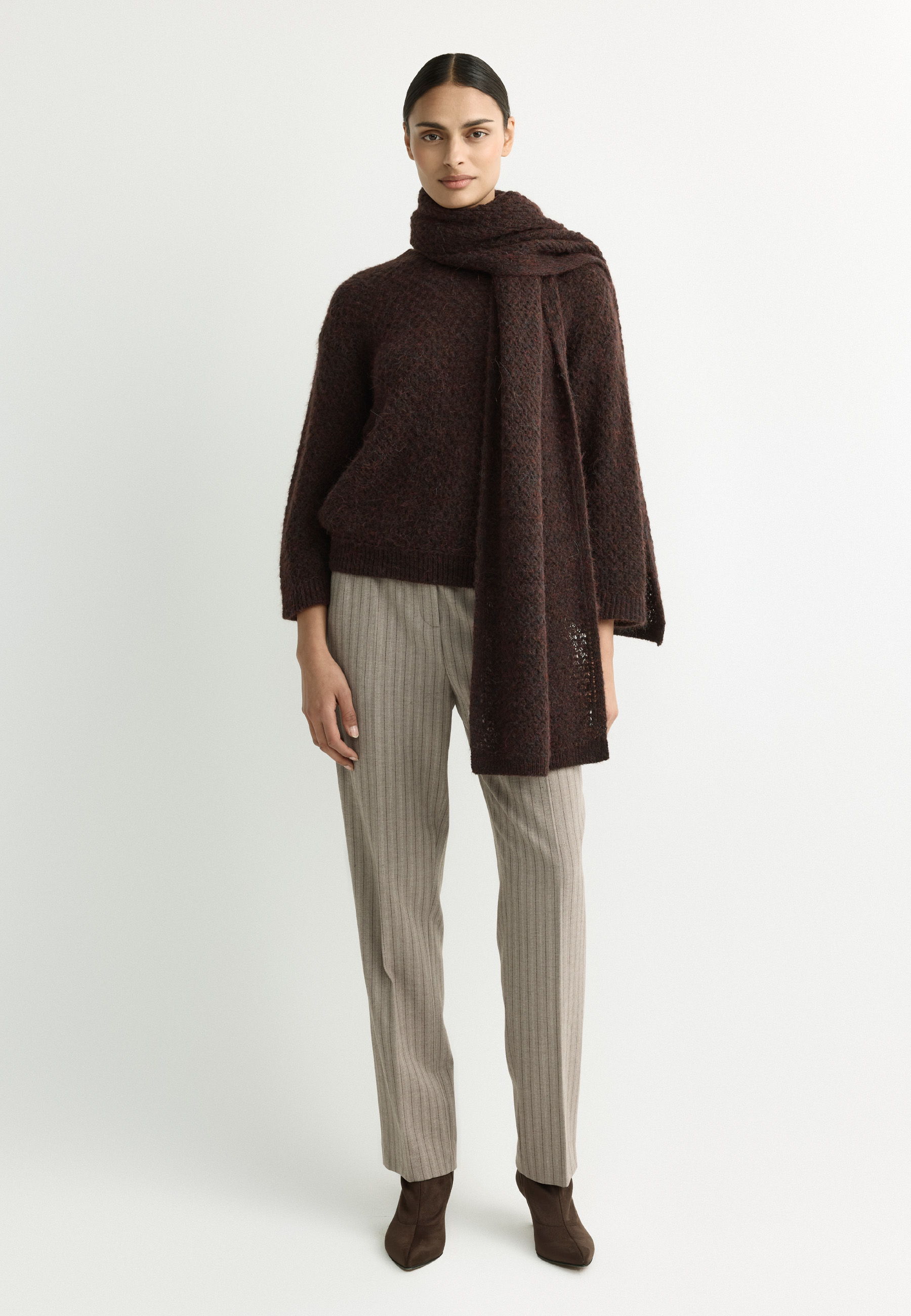 A person wearing a brown sweater and scarf with beige striped pants.