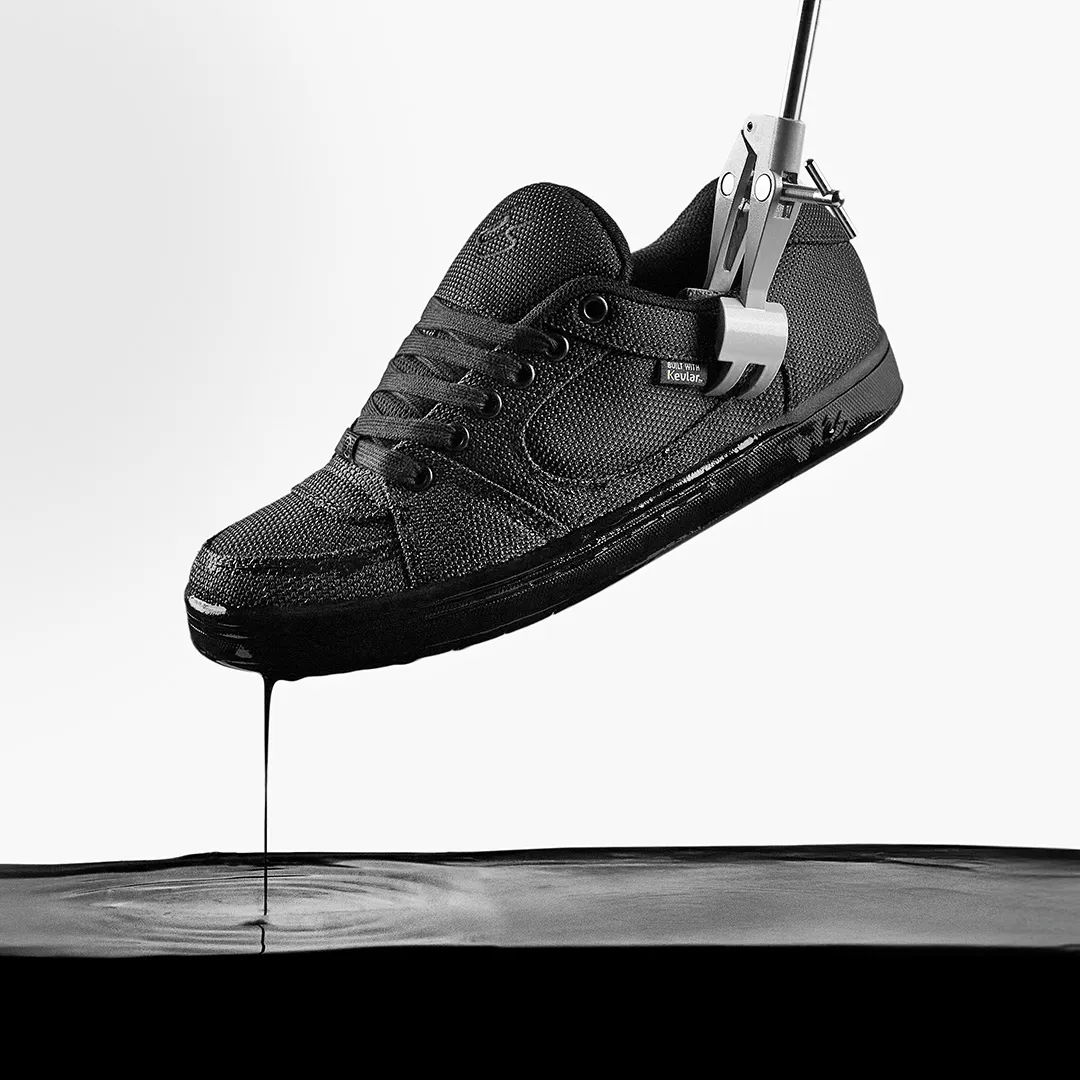 A black sneaker hanging and dripping into a dark liquid below.