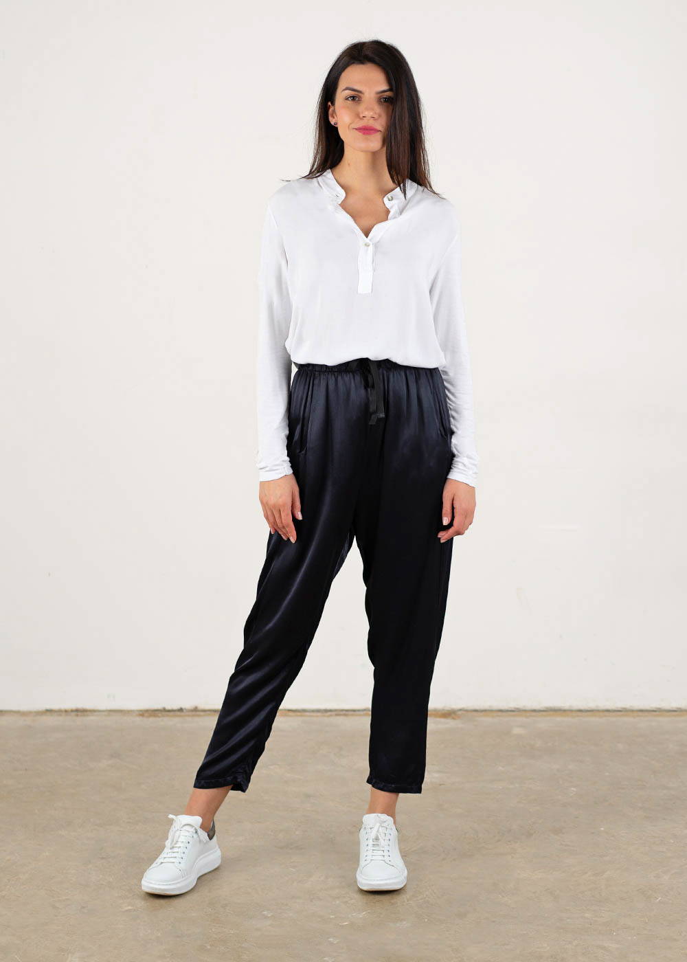 A model wearing a white long sleeve shirt top over blue black satin trousers and white trainers