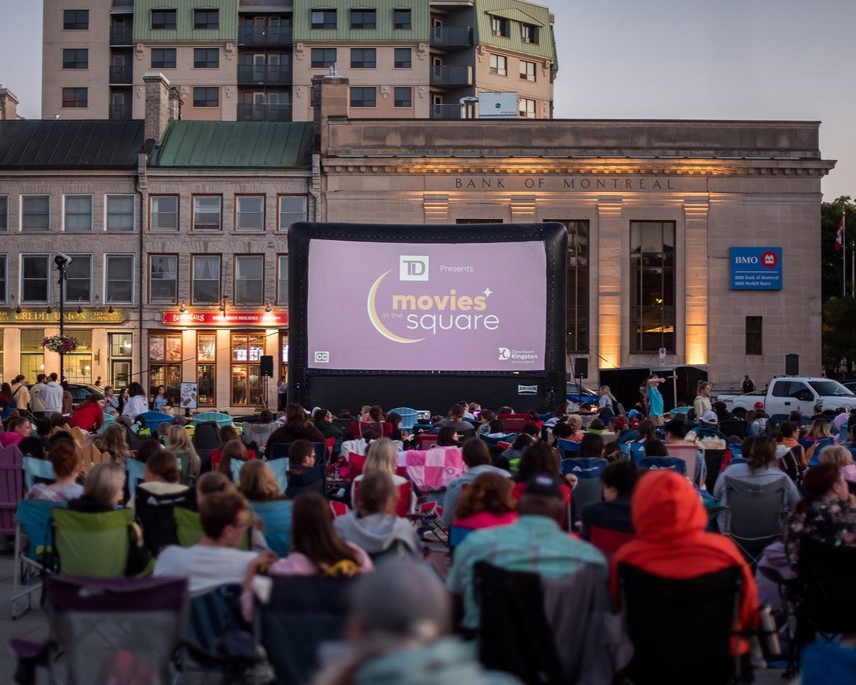Outdoor movie screening with audience seated on chairs in a city setting.