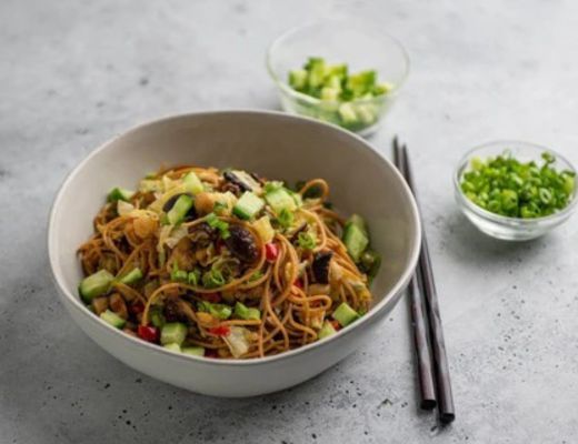 Bowl of noodles with vegetables and two small bowls of chopped green onions.