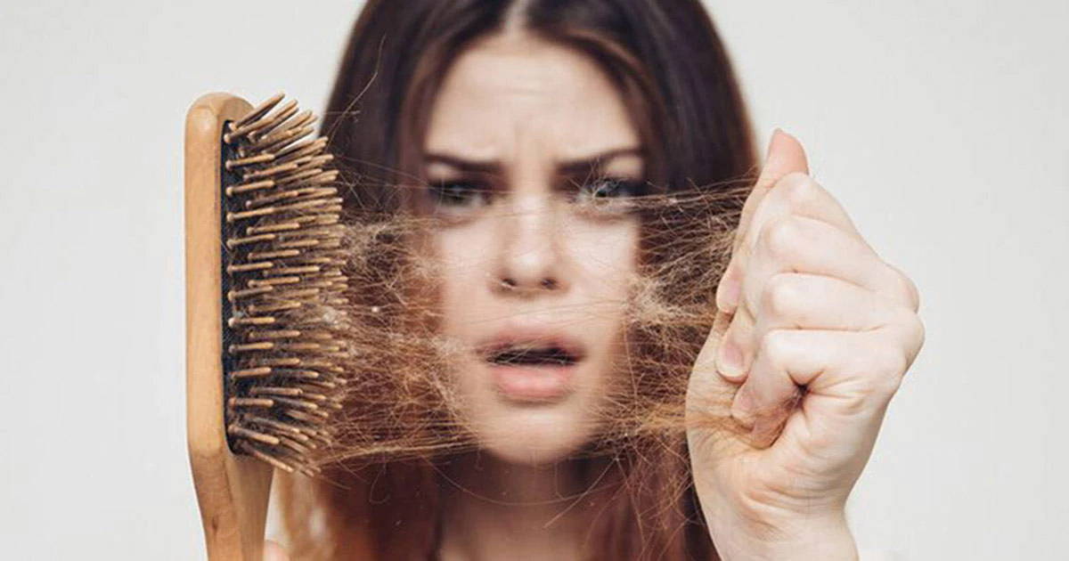 white woman with brown hair has shocked expression while pulling hair out of a tan hairbrush