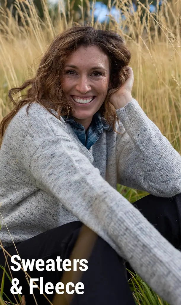 Smiling woman in sweater sitting in tall grass. Text: 