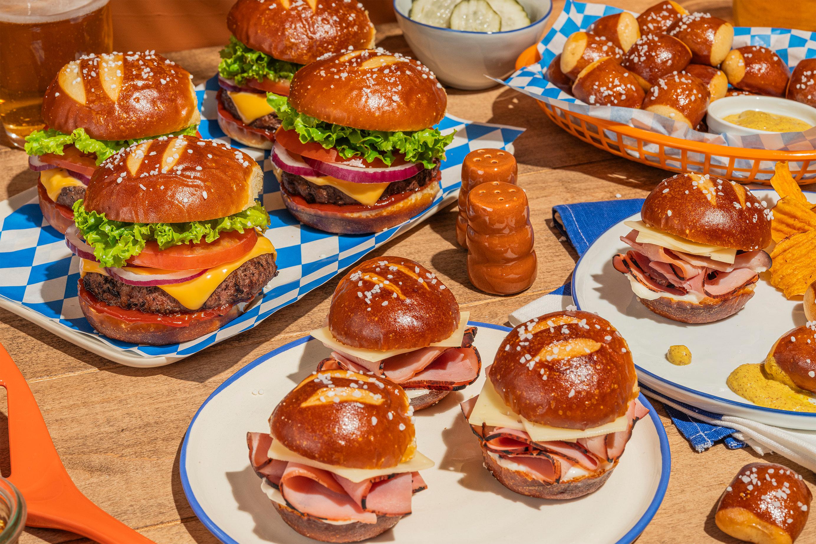 A variety of pretzel burgers and snacks on a wooden table.
