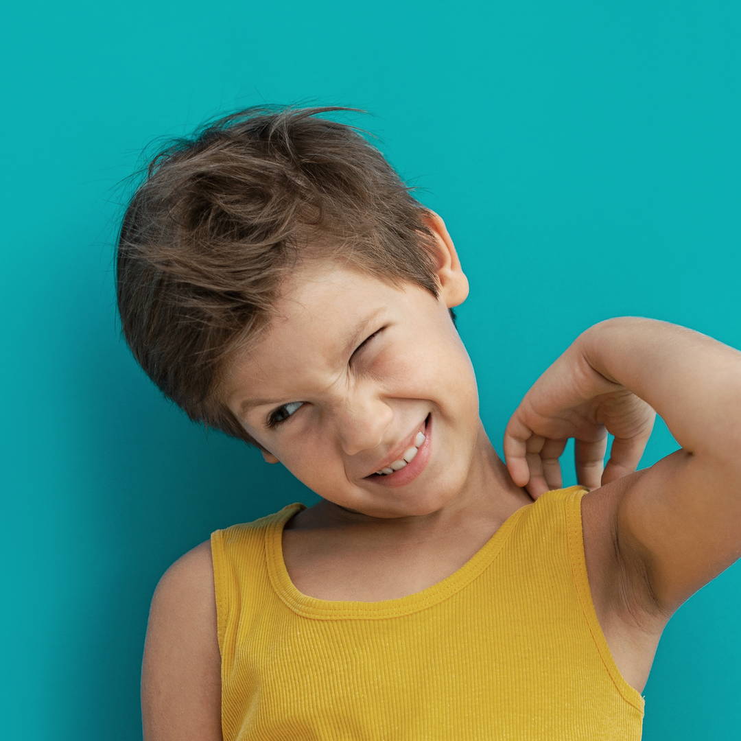 Boy in a yellow vest tilting his head and squinting as he reaches to scratch his shoulder – he could have an allergic rash