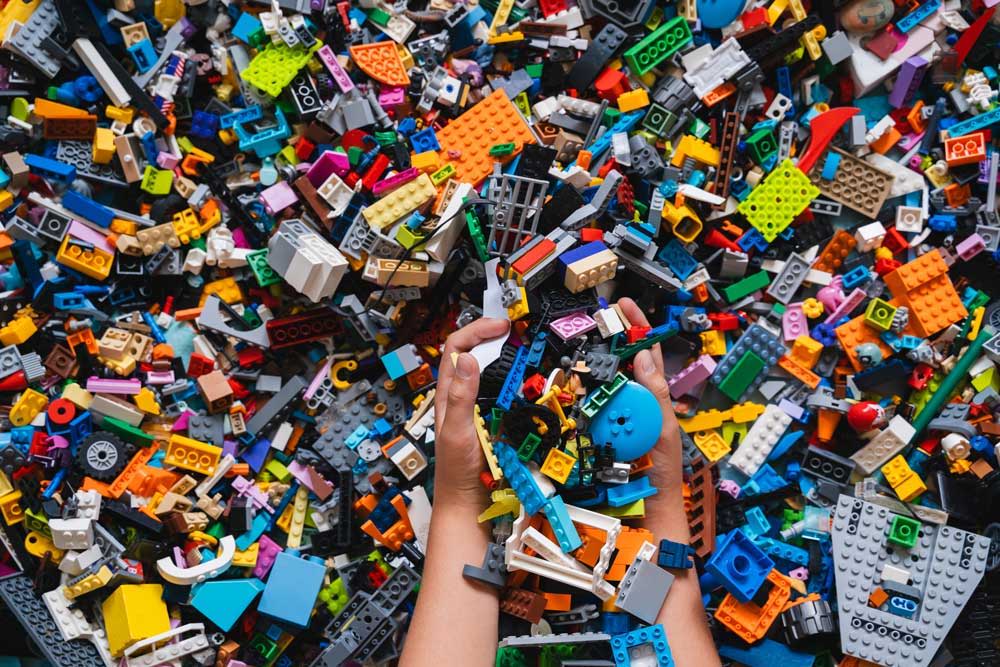 Hands reaching into a colorful pile of assorted Lego bricks.