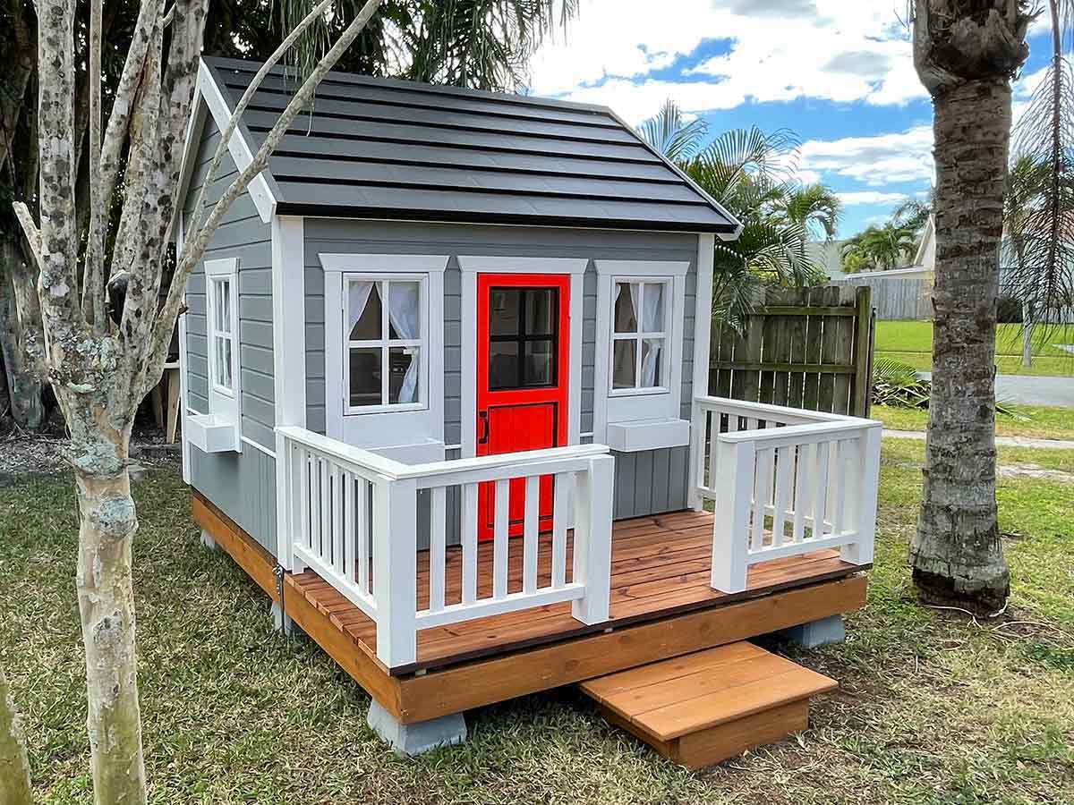 Kids Playhouse in grey color red half glass door and wooden terrace in a backyard by WholeWoodPlayhouses