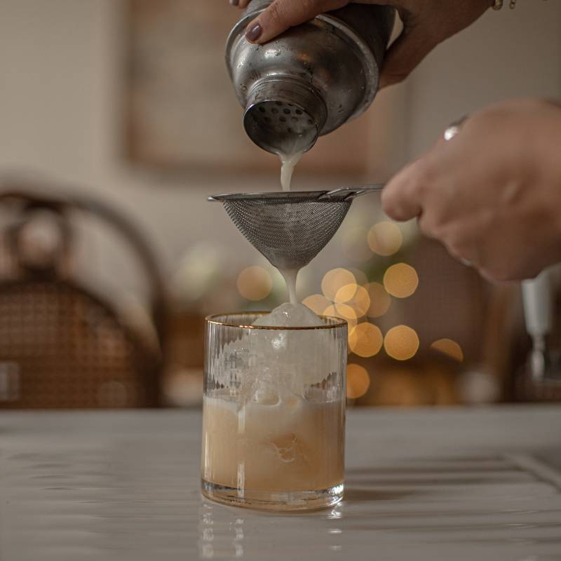 Amaretto Sour being strained into an ice filled cocktail glass