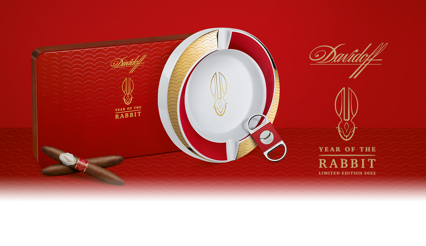 Zwei Davidoff Year of the Rabbit Limited Edition Zigarren gekreuzt vor ihrer roten Kiste liegend, daneben stehen der Year of the Rabbit Aschenbecher und der Year of the Rabbit Cutter.
