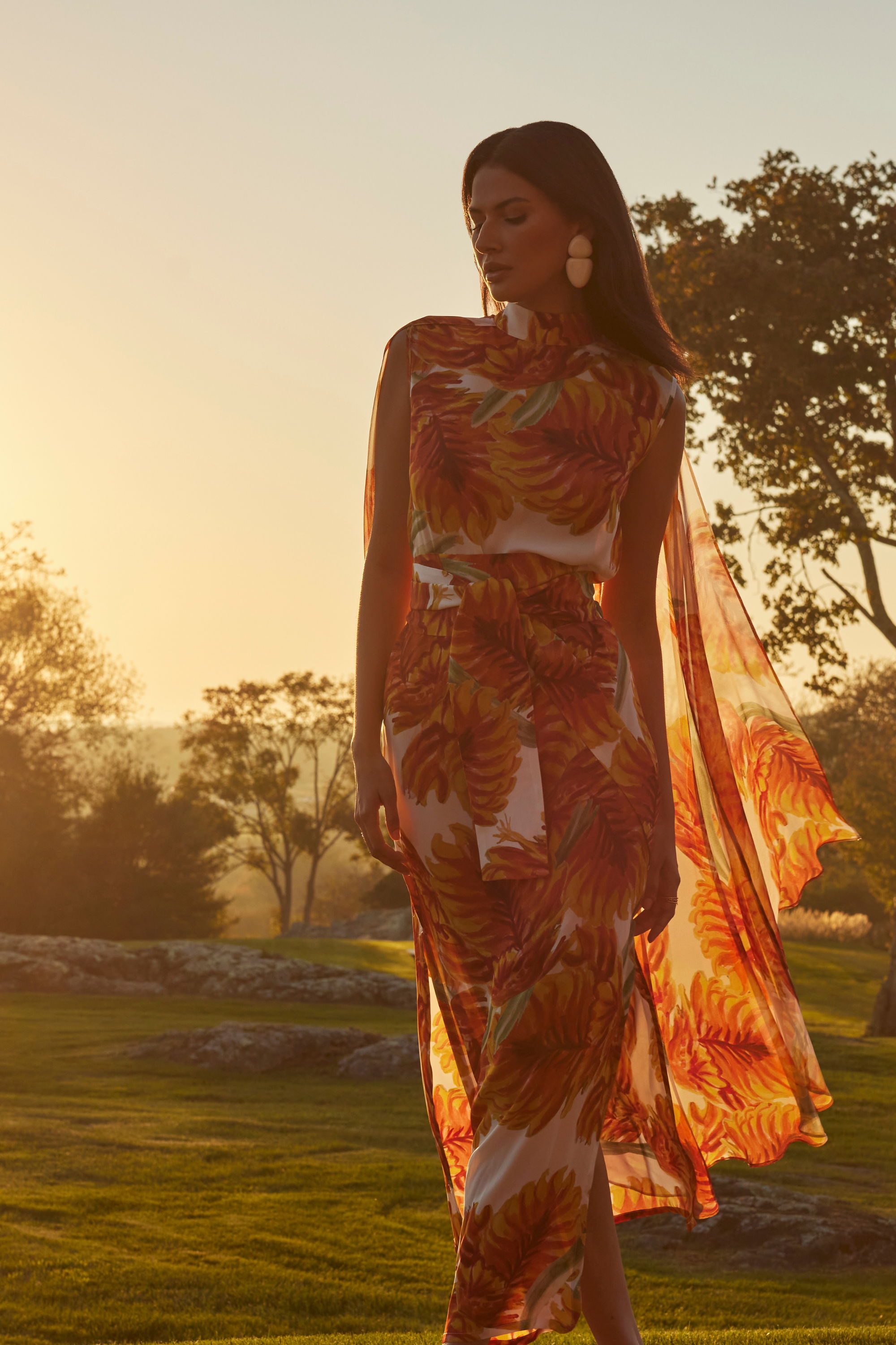 Woman in a floral dress walking at sunset in a serene landscape.