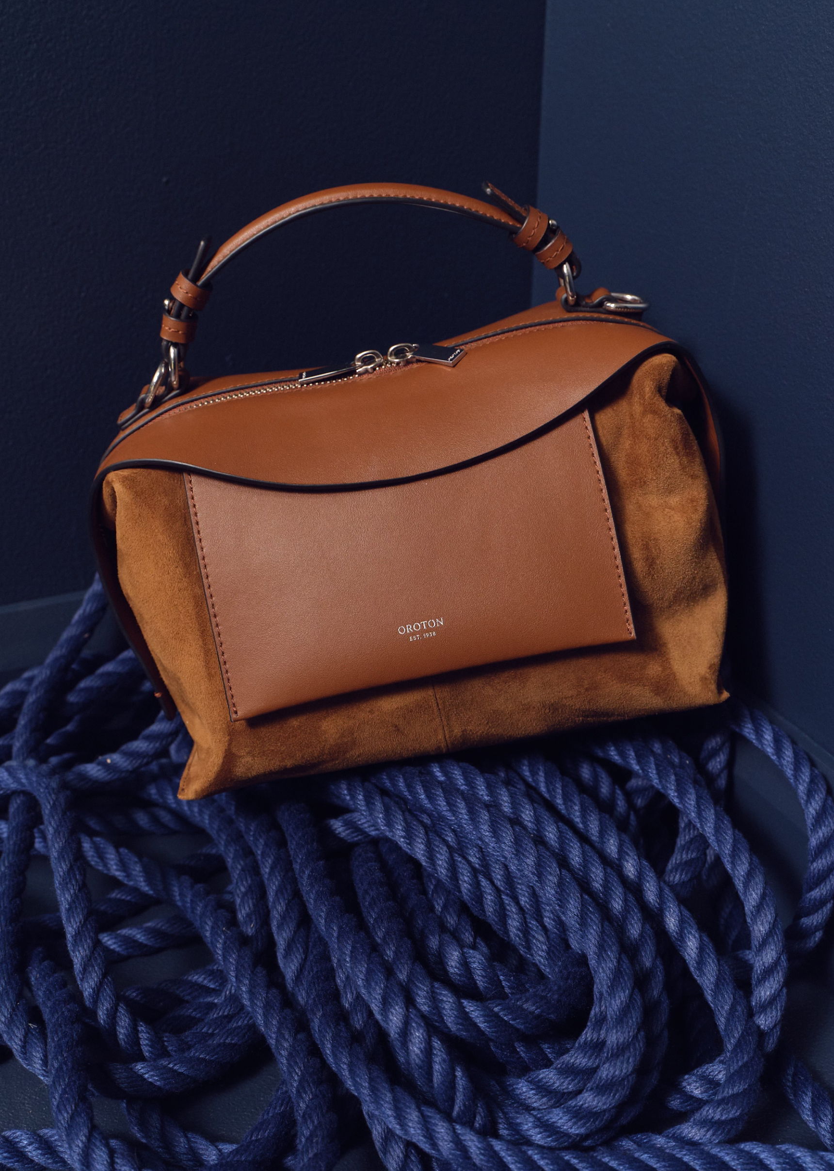 A stylish brown handbag resting on blue ropes against a dark background.