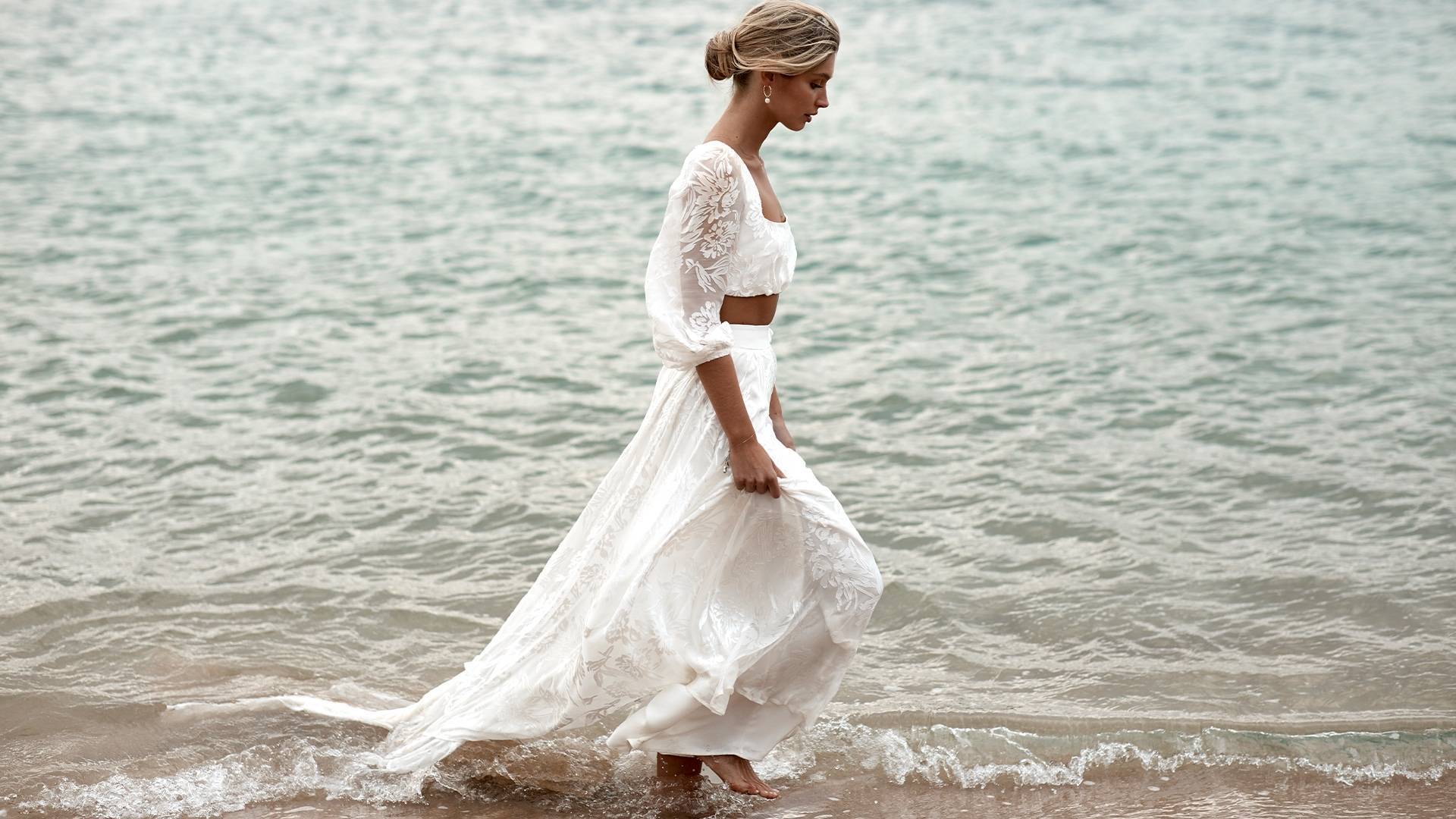  Grace Loves Lace Braut, die am Strand spazieren geht und das Behati-Kleid trägt