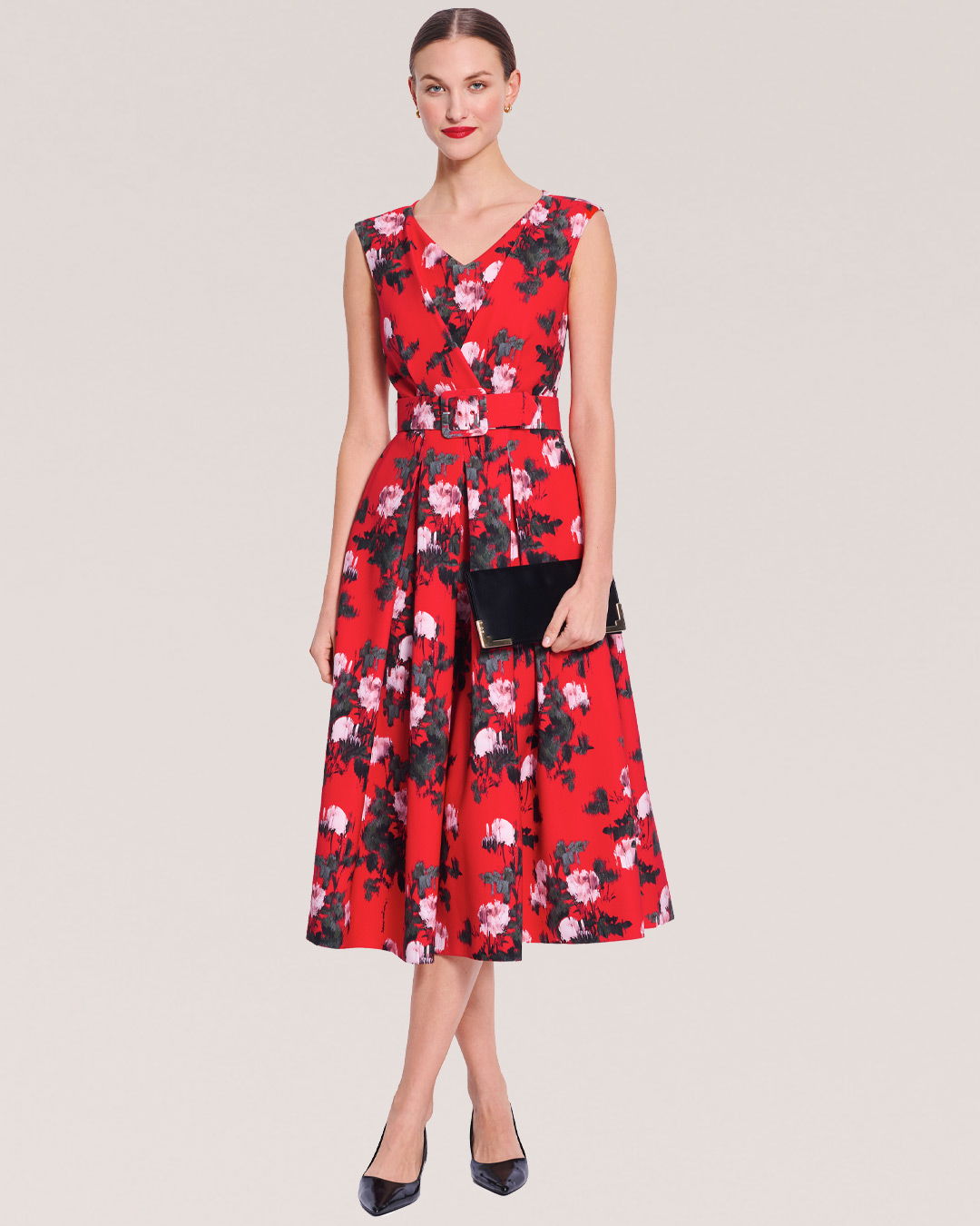 Woman in a floral red dress holding a clutch, standing against a neutral background.