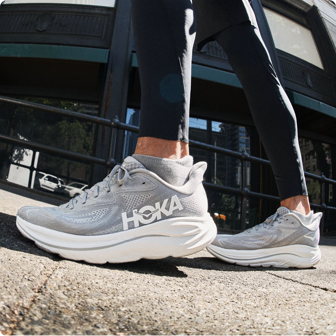 A person wearing HOKA running shoes on a sidewalk.