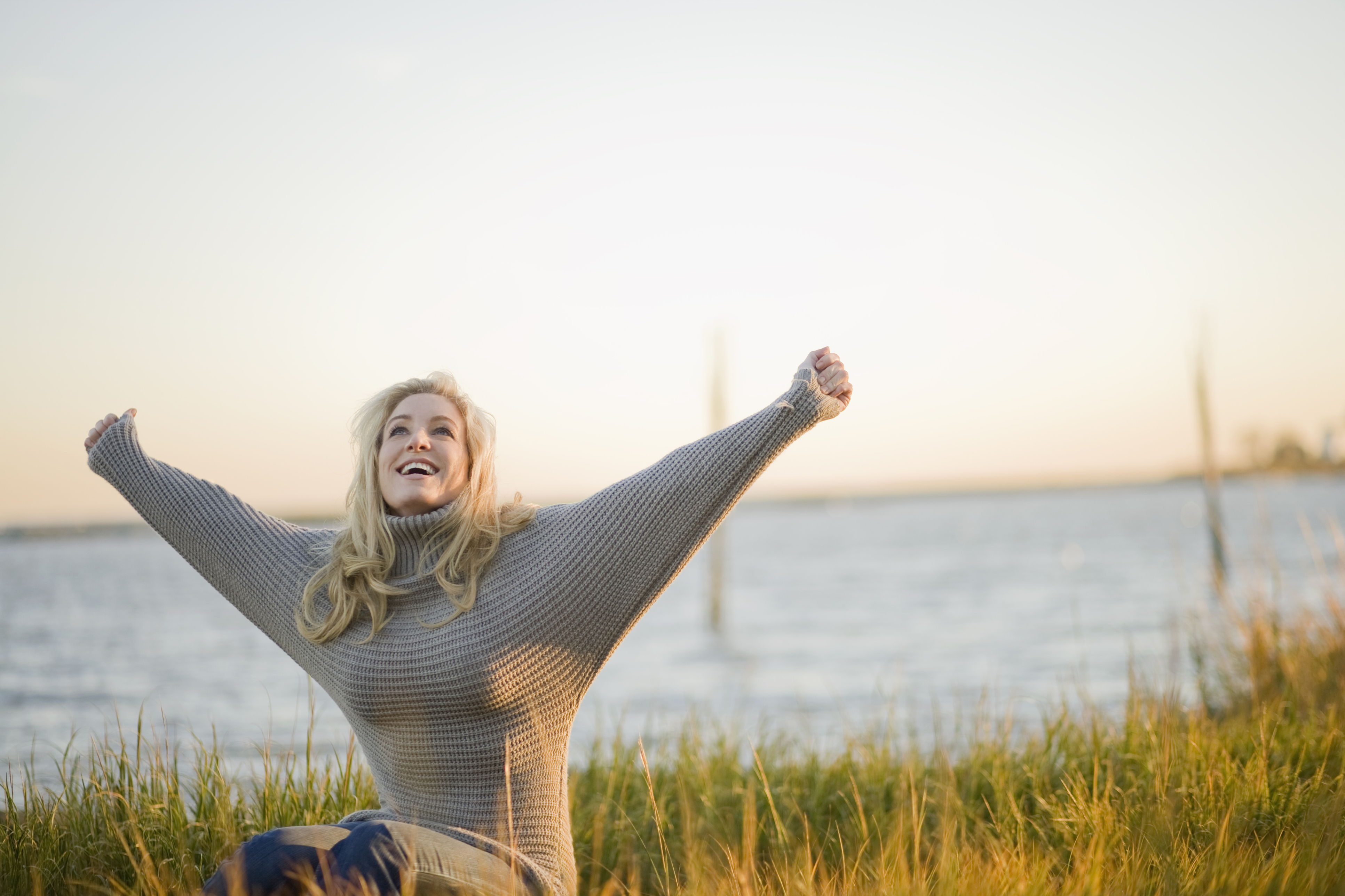 Woman joyfully stretching arms wide by a serene waterfront.