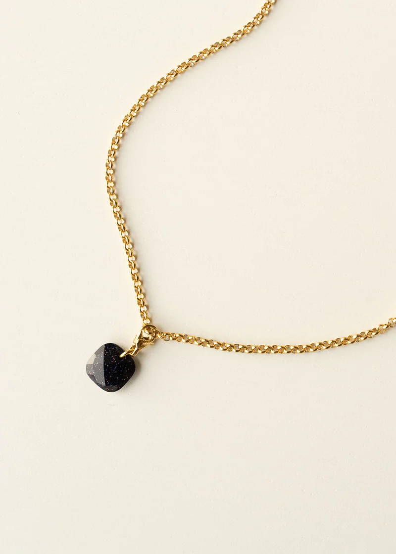 A gold necklace with a black sparkly square pendant