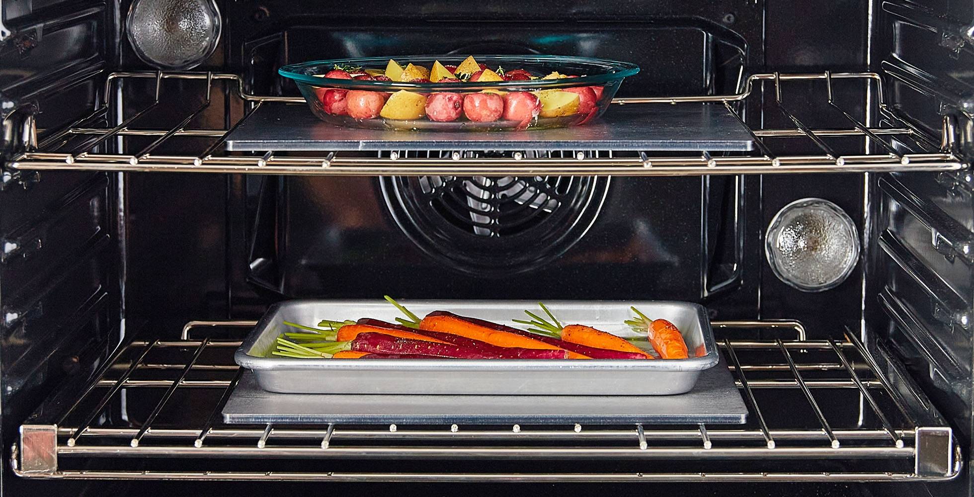 Two Misen Oven Steels cook vegetables on separate racks in one oven — one under a glass baking dish, the other under a metal sheet pan.