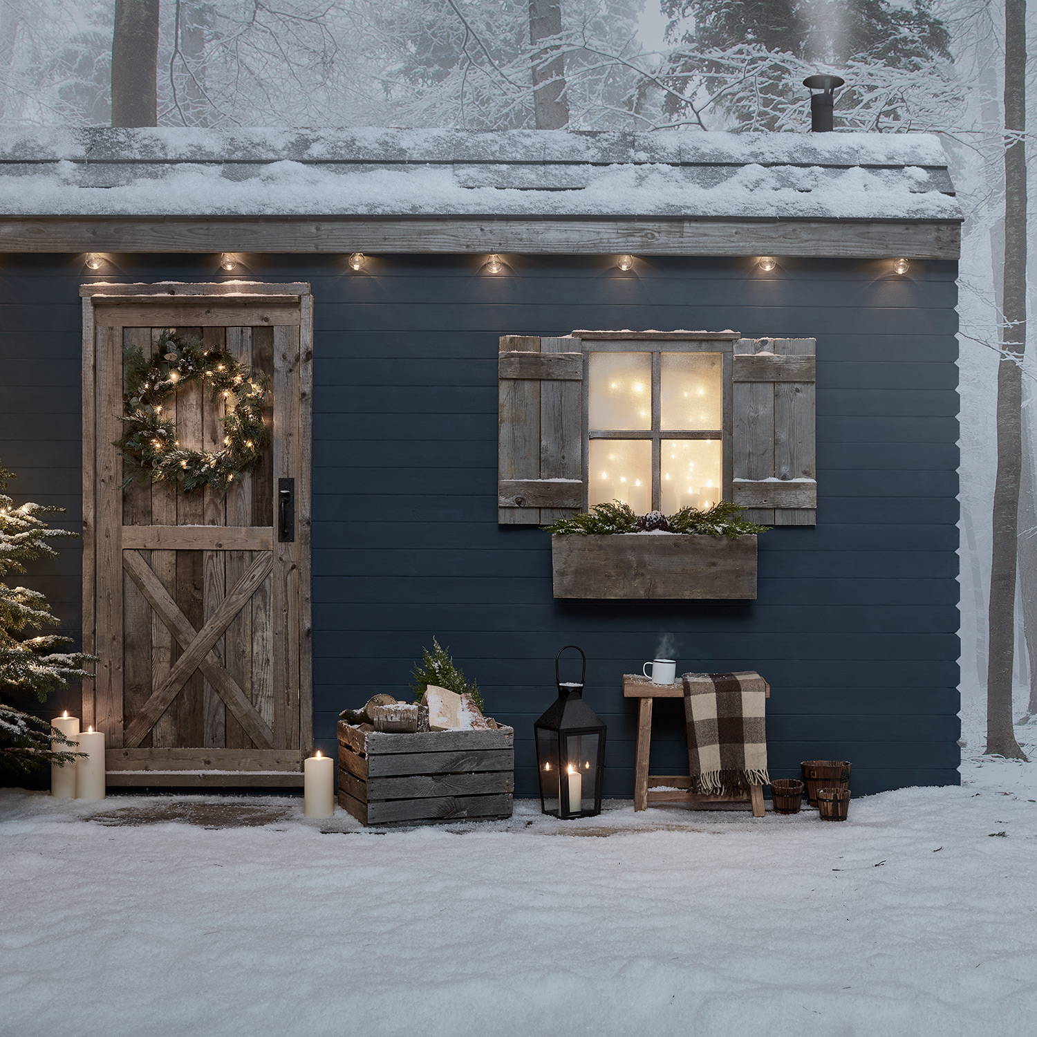 Front of cabin with artificial wreath, garland, candles and a black lantern.