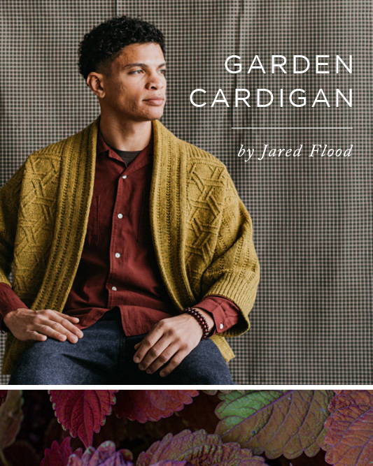 Nico (he/him) models a hand knit lattice textured cardigan while seated agains a gray gingham fabric backdrop. Text overlay reads: Garden Cardigan by Jared Flood.