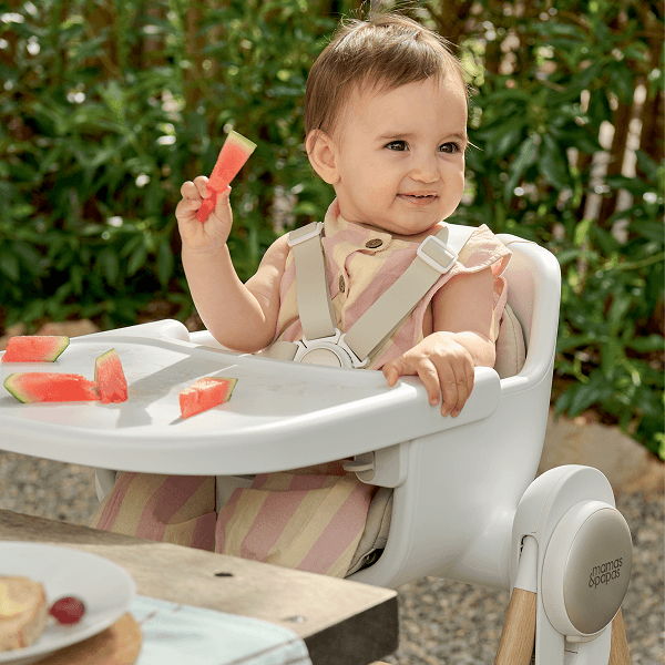 A baby sitting in a high chair holding watermelon pieces.