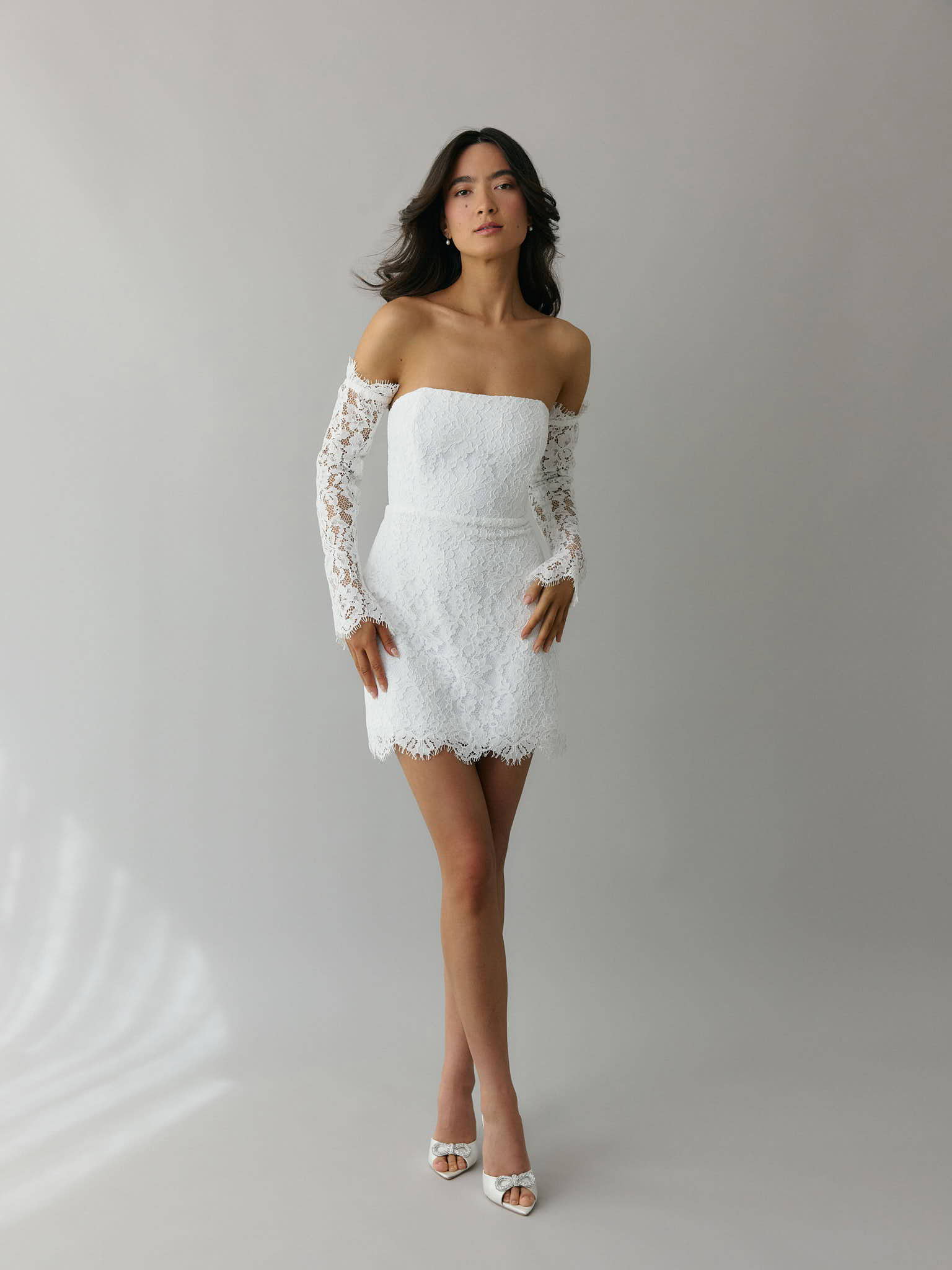 Girl wearing strapless white lace mini bridal event dress with lace sleeves.