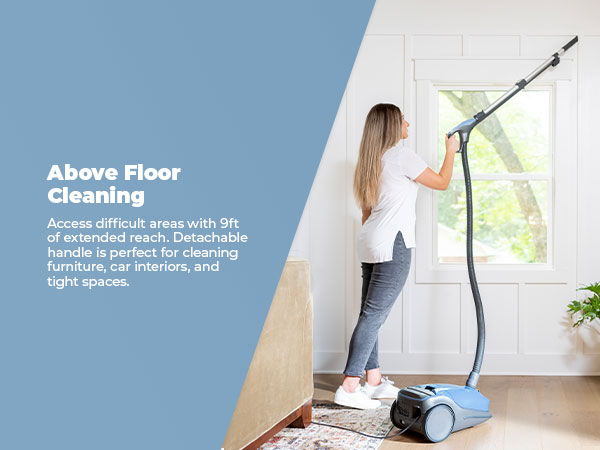 Woman using a vacuum cleaner for above floor cleaning near a window.