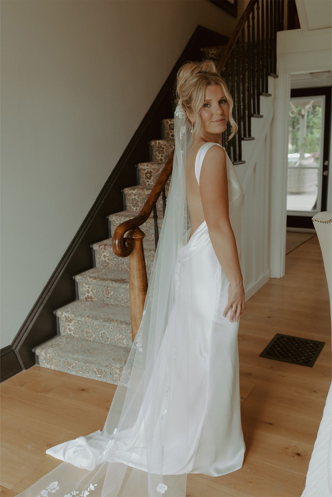 Bride in a white dress with a veil, standing by a staircase.