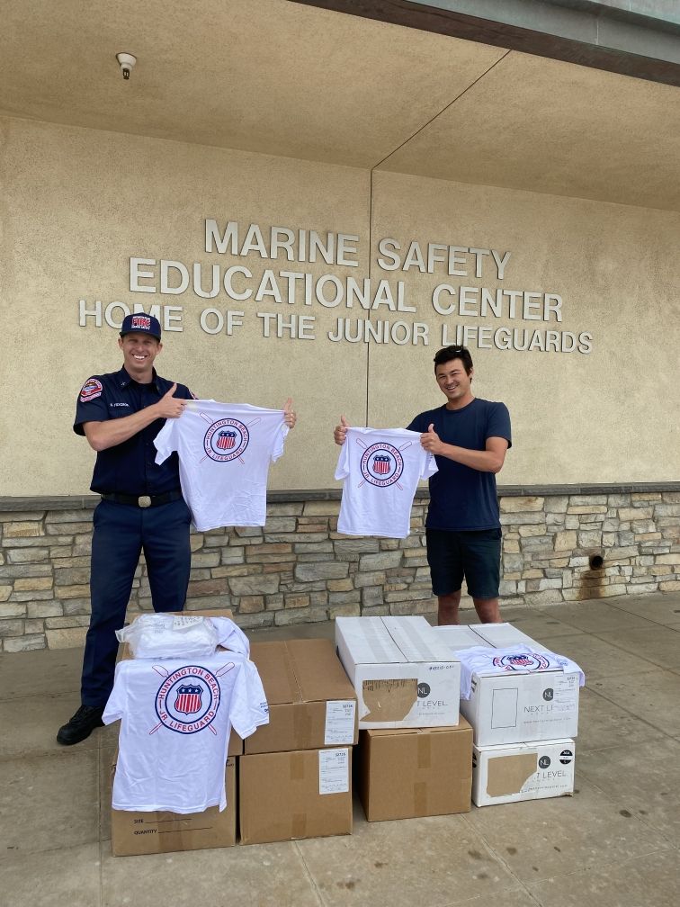 2 people standing in front of Marine Safety Center with boxes of t-shirts